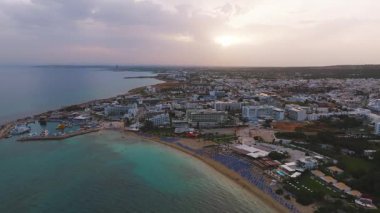 Kıbrıs Rum Kesimi, Ayia Napa üzerindeki hava temizliği marina, kumlu plajlar, temiz sular, beyazlatılmış binalar ve gün batımında tatil beldelerini gösteriyor..