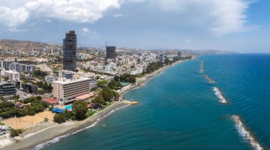 Kıbrıs Rum Kesimi 'nin Limasol kentinin havadan görünüşü, yüksek binaları dalgalı kumsalları, berrak mavi suları ve parçalı bulutlu gökyüzünün altındaki tepelik araziyi gösteriyor..