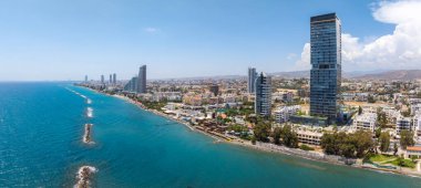 Yüksek binalar, turkuaz sular, dalgalar, yeşil alanlar ve temiz bir gökyüzü altındaki uzak dağların yer aldığı Kıbrıs Rum Kesimi 'nin havadan görünüşü.