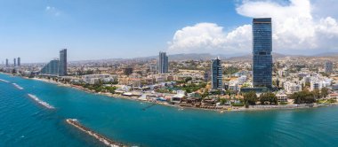 Kıbrıs Rum Kesimi 'nin Limasol kentinin hava görüntüsü, parçalı bulutlu gökdelenler, turkuaz Akdeniz suları, dalgalar ve yuvarlanan tepeleri gösteriyor..