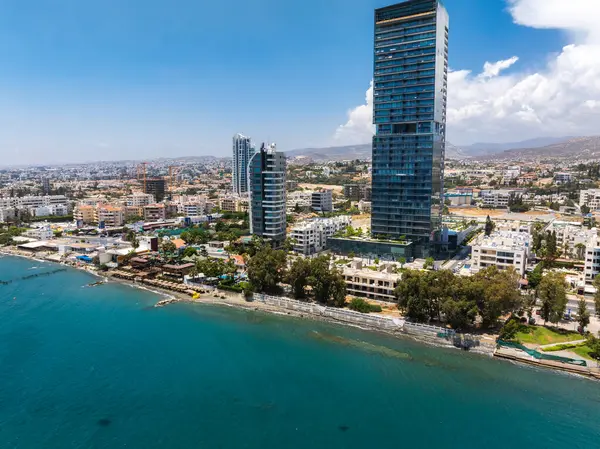 Kıbrıs Rum Kesimi 'nin havadan görünüşü modern bir gökdelen, yüksek binalar, yeşil bir kıyı şeridi, berrak mavi deniz ve parlak bir gökyüzünün altındaki uzak tepeleri gösteriyor..