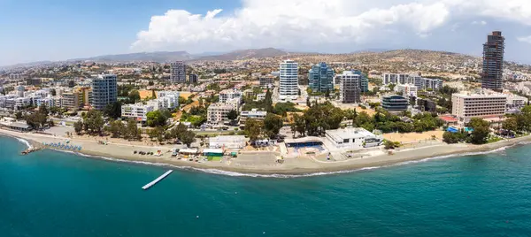 Yüksek binalar, yeşil alanlar, şemsiyeli kumlu bir sahil, bir iskele ve Akdeniz 'in yer aldığı Kıbrıs Rum Kesimi' nin havadan görünüşü.