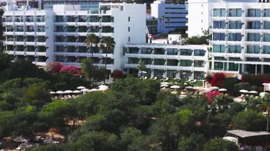 Kıbrıs Rum Kesimi 'nin Ayia Napa kentindeki lüks bir tatil köyünün havadan görünüşü, beyaz binalar, dekoratif köprüsü olan büyük bir havuz, canlı yeşillik ve çiçekleri gösteriyor..