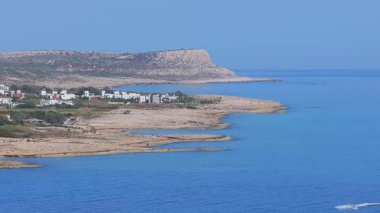 Kıbrıs 'ın Ayia Napa kentinin havadan görünüşü, kumlu plajlar, engebeli uçurumlar, mavi sular, beyaz oteller, yeşillikler ve kayan tepeler.