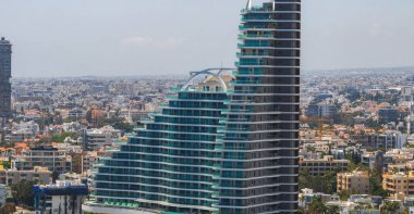 Kıbrıs Rum Kesimi 'nin Limasol kentinin havadan görünüşü, alçak binalar ve kırmızı kiremitli çatılarla çevrili eğimli cam cepheli modern bir gökdelen içeriyor..