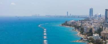 Modern gökdelenler, canlı bir kıyı şeridi, endüstriyel vinçler, kayalık çıkıntılar ve sakin Akdeniz sularının yer aldığı Limasol, Kıbrıs 'ın hava manzarası.