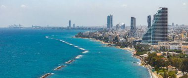 Kıbrıs 'ın Limasol kentinin hava manzarası, modern yüksek binalar, eğri bir yapı, Akdeniz, dalgalar ve uzak bir limanı gösteriyor..