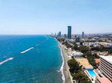 Kıbrıs Rum Kesimi 'nin Limasol kentinin hava manzarasında, yüksek binalar, dalgalı bir kumsal, bir yüzme havuzu ve açık bir gökyüzü altında Akdeniz yer alıyor..