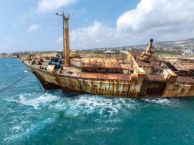 Edro III 'ün enkazı, arka planda tepeler ve kıyı yerleşimi bulunan turkuaz Akdeniz sularıyla çevrili Kıbrıs kayalık kıyı şeridi yakınlarında yer alıyor..