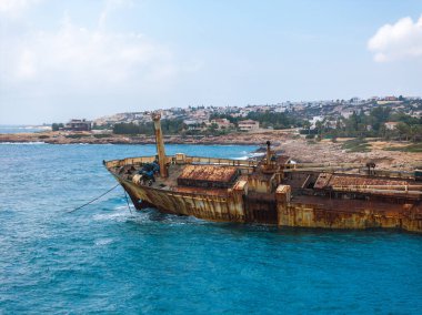 Edro III Batığı, Kıbrıs 'ın kayalık kıyı şeridi yakınlarındaki berrak mavi sularda görünür halat, konut binaları ve dağınık bulutlarla çevrili..