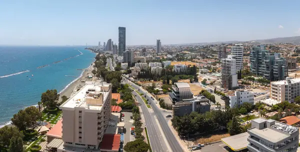 Kıbrıs Rum Kesimi 'nin Limasol kentinin hava manzarasında modern yüksek binalar, yerleşim alanları, kıyı yolu, yeşillik ve dalgalı sularla Akdeniz yer alıyor..