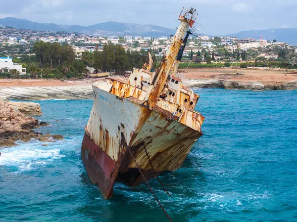 Edro III 'ün gemi enkazı, Kıbrıs' ın turkuaz sularıyla çevrili kayalık kıyıları yakınlarında yatıyor. Arka planda bir kıyı kasabası ve dalgalı tepeler görünüyor..