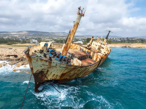 Edro III Batığı, paslı gövdesi, turkuaz dalgaları ve dağılmış tepelerden oluşan kıyı arkaplanı ve dağınık binalarıyla Kıbrıs 'ın kayalık kıyılarına yakın duruyor..