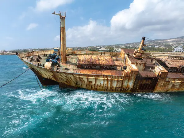 Edro III 'ün enkazı, arka planda tepeler ve kıyı yerleşimi bulunan turkuaz Akdeniz sularıyla çevrili Kıbrıs kayalık kıyı şeridi yakınlarında yer alıyor..