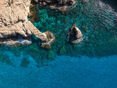 Kıbrıs Rum Kesimi 'nin Ayia Napa kentindeki kayalık kıyı şeridi, sarp kayalıklar, turkuvaz suları ve Akdeniz' deki görünür sualtı kaya oluşumlarıyla hava manzarası.