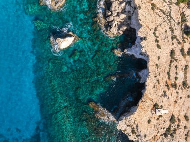 Engebeli bej kayalıkların, turkuaz suların, kayalık çıkıntıların ve Kıbrıs Rum Kesimi 'nin Ayia Napa kentindeki uçurumun kenarındaki küçük beyaz yapının havadan görüntüsü..
