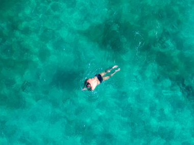 Kıbrıs Rum Kesimi 'nin Ayia Napa kentinde kristal berrak turkuaz suyla yüzen koyu renk mayo giymiş bir yüzücü, derisi desenli deniz yatağı altında görülebiliyor..