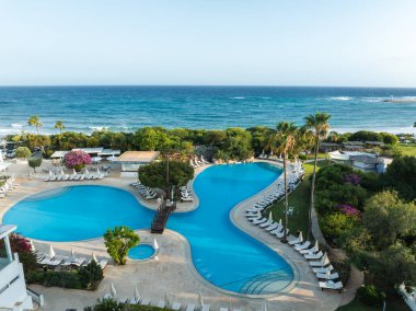 Kıbrıs Rum Kesimi 'nin Ayia Napa kentindeki bir tatil beldesinde büyük bir havuz, ahşap bir köprü, beyaz şezlonglar, palmiye ağaçları ve Akdeniz manzarası bulunuyor..