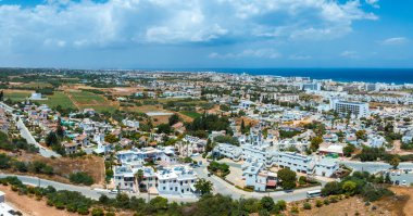 Kıbrıs Rum Kesimi 'nin Ayia Napa kentinin hava manzarası, beyazlatılmış binaları, lüks tatil beldelerini, açık arazileri ve güneşli gökyüzünün altındaki Akdeniz' i gösteriyor..
