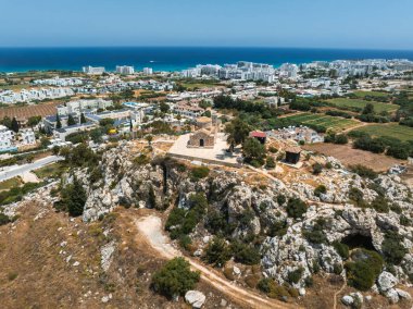 Kıbrıs 'ın Ayia Napa kentindeki kayalık bir tepenin üzerindeki St. Elias Kilisesi' nin hava manzarası, modern tatil beldeleri, yeşil alanlar, kumlu plajlar ve Akdeniz.