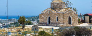 Geleneksel Akdeniz taşı çatılı ve kemerli pencereli Aziz Elias Kilisesi Ayia Napa, yeşillik ve deniz manzaralı yüksek bir alana kurulmuştur..