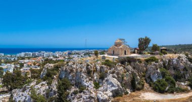 Kıbrıs Rum Kesimi 'nin Ayia Napa kentindeki kayalık bir tepedeki St. Elias Kilisesi' nin hava manzarası, arka planda yeşillik, modern binalar ve Akdeniz ile çevrili..