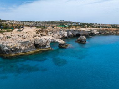 Ayia Napa kıyı şeridi boyunca doğal deniz mağaraları ve kemerleri olan engebeli kireçtaşı aşk uçurumları Akdeniz suları ve dağınık yeşillik.
