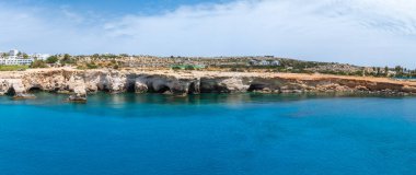 Kıbrıs Rum Kesimi 'nin Ayia Napa kentindeki kireçtaşı kayalıkları, turkuaz Akdeniz suları, beyazlatılmış binalar ve kuru kayalık bir manzarayla kıyı manzarası.