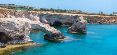 Doğal aşk kemeri ve mağaraları olan engebeli kireçtaşı kayalıkları, Kıbrıs 'ın Ayia Napa kentinde kristal berrak turkuaz sularıyla buluşuyor ve kayaların yanında bir yüzücü bulunuyor..
