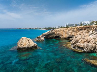 Turkuaz sular, Kıbrıs Rum Kesimi 'nin Ayia Napa kentinde deniz mağaraları ile engebeli kireçtaşından kayalıklarla buluşuyor. Modern beyaz lüks oteller kıyı şeridini canlı mavi gökyüzünün altına dizerler..