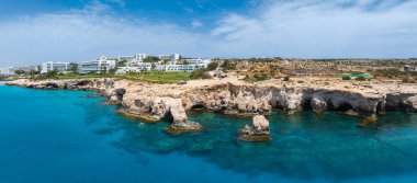 Kıbrıs Rum Kesimi 'nin Ayia Napa kentinin hava manzarası, kireçtaşı kayalıkları, deniz mağaraları, turkuaz suları, lüks tatil beldeleri, beyaz binalar ve yemyeşil alanları gösteriyor..