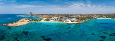 Kıbrıs Rum Kesimi 'nin Ayia Napa kentinin hava manzarasında turkuaz sular, güneşli kumlu plajlar, lüks tatil beldeleri, yüksek binalar ve doğal manzaralar görülüyor..
