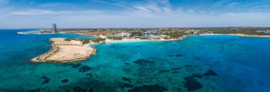 Kıbrıs Rum Kesimi 'nin Ayia Napa kentinin havadan görünüşü, Nissi Sahili' ni, turkuaz suları, lüks tatil beldeleri, güneş pansiyonları, engebeli kıyı şeridi ve sualtı kaya oluşumlarını gösteriyor..