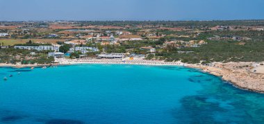 Kıbrıs Rum Kesimi 'nin Ayia Napa kentindeki hilal şeklinde deniz manzaralı turkuaz sular, güneş pansiyonları, şemsiyeler, lüks tatil beldeleri ve yemyeşil alanlar.