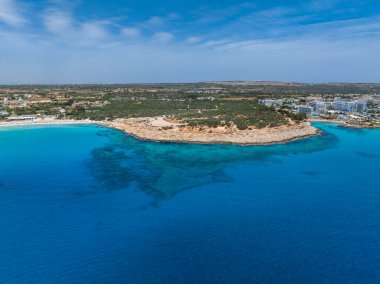 Kıbrıs 'ın Ayia Napa kentindeki kayalık bir yarımadanın havadan görünüşü turkuaz sular, kumlu plajlar, lüks oteller, yeşillik ve açık mavi gökyüzü ile çevrili..