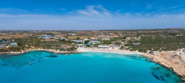 Aerial view of Ayia Napa, Cyprus, showing turquoise waters, sandy beaches with sun loungers, anchored boats, luxury resorts, and green areas.
