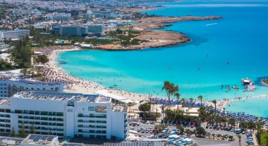 Kıbrıs Rum Kesimi 'nin Ayia Napa kentindeki Nissi Plajı' nın turkuaz sular, kumlu kıyılar, lüks tatil beldeleri, güneş pansiyonları ve su faaliyetlerinden keyif alan insanlar ile hava manzarası.