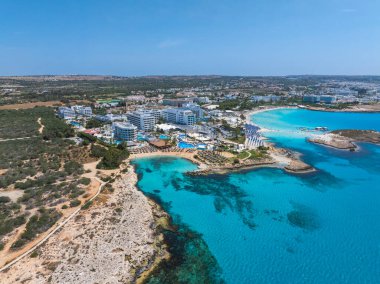 Ayia Napa 'nın turkuvaz suları, kumlu plajları, lüks tatil beldeleri, güneş pansiyonları, kayalık çıkıntıları ve yüzen insanlarla dolu kıyı şeridinin havadan görüntüsü..
