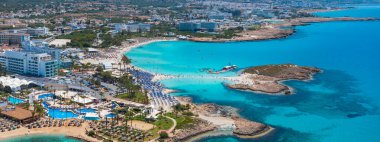 Kıbrıs Rum Kesimi 'nin Ayia Napa kentinde, Nissi Sahili' nin turkuaz suları, lüks tatil beldeleri, güneşlikler, şemsiyeler, botlar ve yemyeşil alanları bulunuyor..