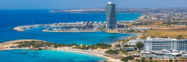 Kıbrıs 'ın Ayia Napa kentinin havadan görünüşü, Nissi Sahili, turkuaz sular, yatlı bir marina, lüks tatil beldeleri ve yemyeşil verimli kentsel alanlar.