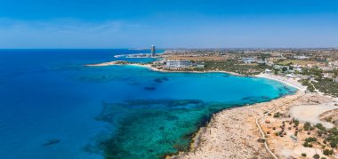 Kıbrıs Rum Kesimi 'nin Ayia Napa kentinin havadan görünüşü Nissi Sahili, turkuaz sular, kumlu kıyı şeridi, kayalık çıkıntılar, lüks oteller ve denizde küçük tekneler gösteriyor..