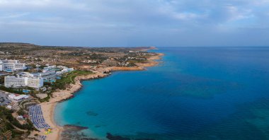 Kıbrıs 'ın Ayia Napa kentinin hava manzarasında turkuaz sular, güneşli kumlu plajlar, lüks tatil beldeleri, yemyeşil alanlar ve engebeli uçurumlar görülüyor..