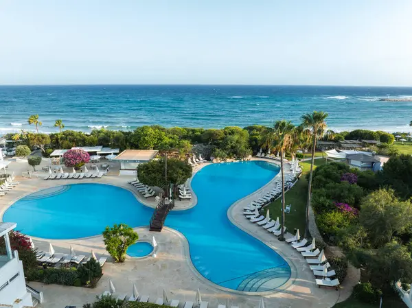 Kıbrıs Rum Kesimi 'nin Ayia Napa kentindeki bir tatil beldesinde büyük bir havuz, ahşap bir köprü, beyaz şezlonglar, palmiye ağaçları ve Akdeniz manzarası bulunuyor..