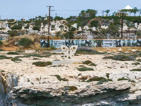 Ayia Napa 'da kayalık bir manzara. Kelebek şekilli bir heykel, yakınlardaki sanat tesisleri, beyaz bir gölgelik ve sahnede seyrek bir bitki örtüsü..