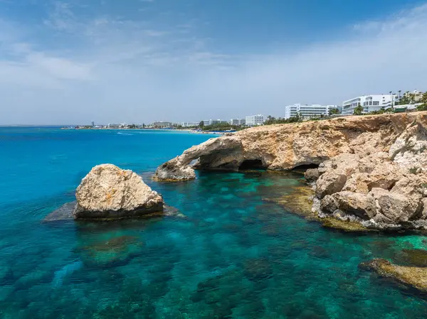 Turkuaz sular, Kıbrıs Rum Kesimi 'nin Ayia Napa kentinde deniz mağaraları ile engebeli kireçtaşından kayalıklarla buluşuyor. Modern beyaz lüks oteller kıyı şeridini canlı mavi gökyüzünün altına dizerler..