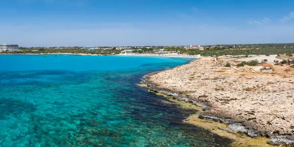 Kıbrıs Rum Kesimi 'nin Ayia Napa kentinin havadan görünüşü turkuaz suları, kayalık kıyı şeridi, kumlu Nissi Sahili, lüks tatil beldeleri, yemyeşil alanlar ve plaja gidenleri gösteriyor..