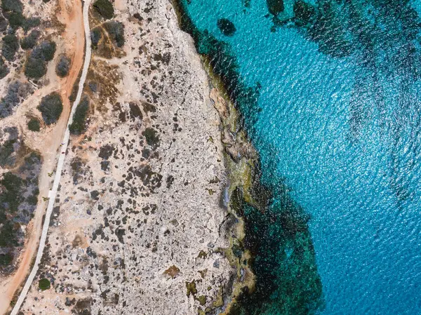 Kıbrıs 'ın Ayia Napa kentinin hava görüntüleri engebeli kayalık arazi, seyrek bitki örtüsü, dolambaçlı bir yol ve canlı turkuaz Akdeniz sularını gösteriyor.