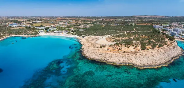 Kıbrıs Rum Kesimi 'nin Ayia Napa kentinin hava manzarasında turkuaz sular, kayalık kıyılar, güneş pansiyonları, yemyeşil alanlar, tatil beldeleri ve kentin altyapısı görülüyor..