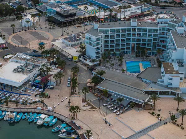 Kıbrıs Rum Kesimi 'nin Ayia Napa kentinin havuz, palmiye ağaçları, tekneleri olan bir marina, dairesel bir plaza ve beyaz kemerli bir binası olan lüks bir oteli gösteren hava manzarası..