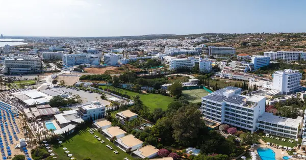 Kıbrıs Rum Kesimi 'nin Ayia Napa kentinin hava manzarasında lüks oteller, yeşil alanlar, yüzme havuzları, güneşlikler, kentsel binalar ve Akdeniz kıyı şeridi görülüyor..